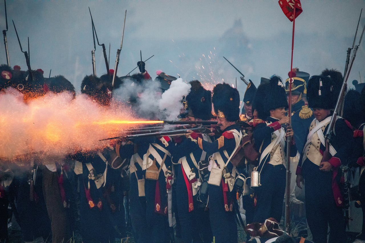 Image of French soldiers in old uniforms from the Napolenic era firing their guns.